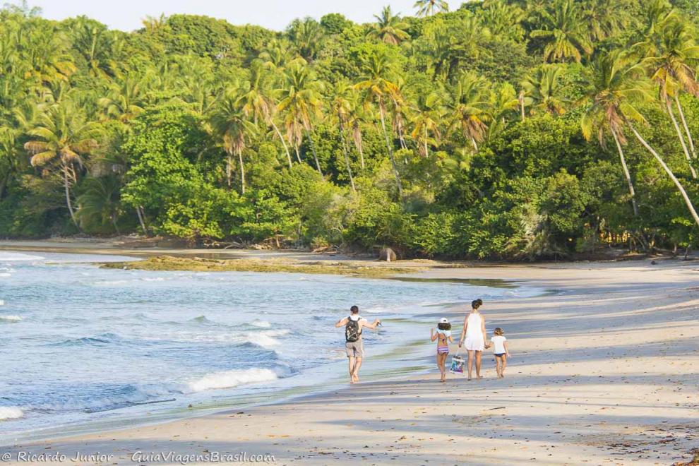 Imagem de uma família andando na beira do mar, indo embora da Praia da Boca da Barra.